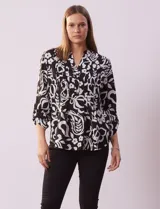Blusa de gasa estampada con diseño geométrico multicolor, cuello a la base con escote en V y abertura frontal con botones. Presenta detalle de plisado en la parte delantera y mangas largas con sistema de ajuste mediante presilla y botón.