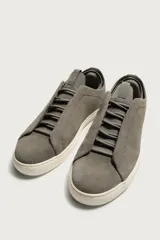 Zapatilla de piel con acabado en serraje de color gris, diseño de cordones ocultos y suela de goma en contraste de color blanco.