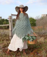 Poncho tejido a mano de lana merino color verde, con diseño de punto texturizado con bodoques y terminación de flecos en el ruedo.