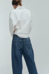 Jean tobillero de cinco bolsillos en denim de algodón rígido, con piernas de volumen curvo, corte estándar y tiro alto con cierre de botones.