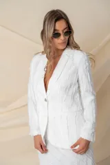 Blazer de corte sastre en color blanco, confeccionado en crepé satén con detalles de flecos de seda en toda la prenda. Presenta solapas clásicas, cierre frontal con botón de nácar y dos bolsillos laterales tipo ojal.