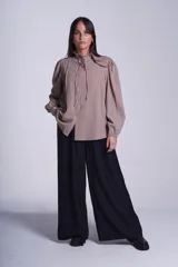 Camisa de color azul con cuello alto decorado con volados y lazo de ajuste. Presenta tablas decorativas en los hombros, cierre frontal con botones de nácar y mangas largas con puños elásticos que generan un efecto abullonado.