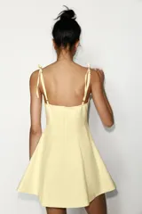 Vestido corto color amarillo pálido, con escote corazón, tirantes finos ajustables con detalle de lazos y falda acampanada.