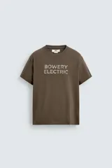 Camiseta de manga corta y cuello redondo, color marrón oscuro, con estampado frontal que dice "BOWERY ELECTRIC" en tipografía desgastada.