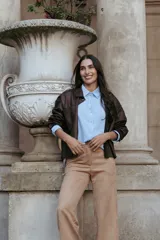 Chaqueta de cuero sintético color marrón oscuro, con cuello camisero, cierre frontal con botones metálicos y bolsillos laterales.