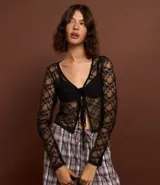 Blusa de manga larga confeccionada en encaje floral transparente, con escote en V y cierre frontal mediante lazos.