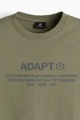 Remera de algodón verde militar con cuello redondo y estampado frontal con texto en color gris.