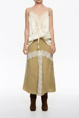 Falda midi de corte evasé en color beige, con aplicaciones de encaje blanco en forma de cruz y laterales. Cuenta con cierre invisible en la parte posterior.