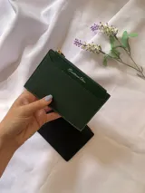 Tarjetero de diseño rectangular con cierre superior, confeccionado en material texturizado color verde con detalles en cuero sintético. Incluye el nombre de la marca grabado en el frente.
