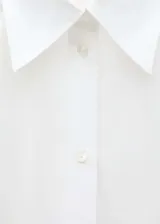 Camisa blanca de popelina de algodón, corte amplio, cuello camisero clásico y cierre frontal con botones.