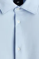 Camisa de manga larga en tejido elástico de mezcla de algodón, con cuello italiano, cierre frontal de botones y puños ajustables. Presenta un corte entallado slim fit y bajo redondeado.