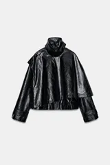 Chaqueta de efecto piel en color negro con cuello subido y bufanda desmontable integrada mediante botones. Presenta manga larga con trabillas ajustables en los puños, cierre frontal con cremallera y bolsillos laterales ocultos en las costuras. El diseño incluye un bajo con elástico en la espalda y forro interior.