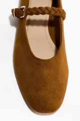 Ballerinas de gamuza color marrón con punta redondeada y tira trenzada ajustable en el empeine con hebilla metálica.