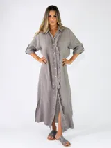 Vestido largo de lino gris, estilo camisero, con mangas tres cuartos con presilla para arremangar, cierre frontal de botones y detalles de volados a lo largo de la botonera.
