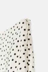 Falda midi fluida de tiro medio en color crudo con estampado de lunares negros, de corte evasé y caída ligera.
