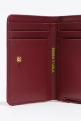 Billetera compacta de estructura blanda en color turquesa, con cierre de cremallera superior y logo metálico dorado en el frente.