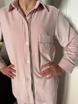 Pijama de dos piezas color rosa pálido, confeccionado en terciopelo. La camisa es de manga larga con botones frontales y bolsillo en el pecho. El pantalón es de corte recto con cintura elástica.