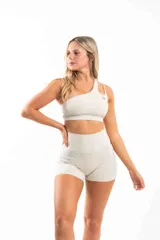 Conjunto deportivo color crema compuesto por un top asimétrico con un solo tirante y shorts de tiro alto con bolsillos laterales.