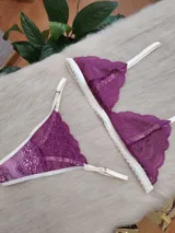 Conjunto de lencería compuesto por un bralette triangular y una tanga, confeccionados en encaje color fucsia con terminaciones y breteles en color crema. El bralette presenta un diseño sin aros con bordes festoneados, mientras que la tanga cuenta con tiras laterales regulables.