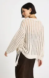 Sweater beige de punto calado con escote en V profundo, mangas largas holgadas con puños acanalados y detalle de lazo ajustable en el lateral.