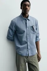 Camisa de corte relajado confeccionada en una mezcla de lyocell y algodón con efecto lavado. Presenta cuello solapa, manga larga con puños abotonados, bolsillo de plastrón en el pecho y cierre frontal con botones.