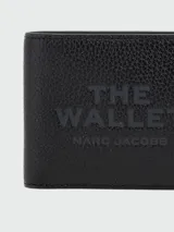 Billetera Marc Jacobs modelo The Billfold, color negro, con diseño plegable de cuero texturizado y estampado frontal en relieve con el texto "The Wallet" y la marca.