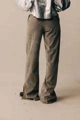 Pantalón de tiro medio, corte recto, color gris, confeccionado en tela agamusada con cierre frontal, botón en la cintura y tajos en el ruedo.
