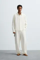 Pantalón de corte relajado confeccionado en tejido de cáñamo color blanco roto. Presenta cintura elástica con cordón interior ajustable, cierre frontal con botones, bolsillos laterales y un bolsillo trasero de plastrón.