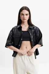 Camisa de manga corta confeccionada en cuero sintético color bordó, con cuello clásico, cierre frontal de botones metálicos y dos bolsillos frontales con solapa.