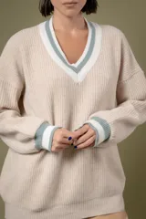 Buzo de punto en color azul marino con escote en V, puños y cuello con detalles en franjas de color turquesa y rojo. Presenta un diseño holgado de manga larga.