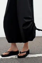 Pantalón culotte de tiro medio, color verde militar, con cintura elástica y bolsillos laterales ocultos. Presenta un diseño de bajo ancho con aberturas ajustables mediante cordones fruncidos en los laterales.