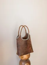 Bolso tipo matera de cuero con textura de reptil, color tostado, con manijas trenzadas y detalles de costura artesanal en los bordes.