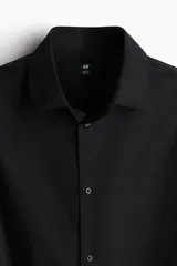 Camisa de vestir negra con cuello italiano, cierre frontal de botones y mangas largas con puños ajustables. Presenta un corte entallado y bajo redondeado.