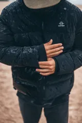 Campera puffer con capucha, color negro, con cierre frontal y diseño acolchado. Presenta un acabado con efecto mojado y logo pequeño en el pecho.