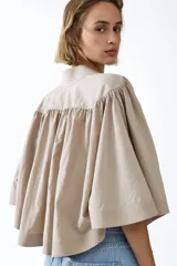 Blusa capa color beige con cuello alto, hombreras y diseño acampanado con frunces.