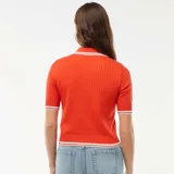Sweater de punto canalé color naranja, de manga corta, con cuello polo blanco y ribetes a rayas blancas en el cuello, puños y dobladillo. Presenta cierre frontal con botones dorados.