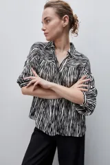Camisa de calce amplio confeccionada en viscosa fluida con estampado animal print tipo cebra en blanco y negro. Presenta cuello camisero, escote en V y mangas largas con puños elastizados, además de frunces en el canesú que aportan volumen.