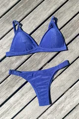 Bikini de dos piezas color marrón, con corpiño triangular fijo con corte bajo el busto, breteles regulables con hebilla y almohadillas desmontables. La bombacha es vedetina con frunce elástico en los costados.