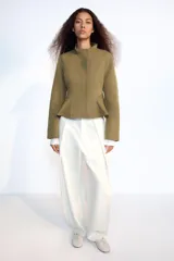 Cazadora entallada Zara color verde militar, con cuello alto, manga larga y bajo acabado en peplum. Cuenta con cierre frontal oculto con cremallera y botones a presión.