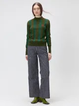 Sweater de punto con diseño de rayas verticales en tonos negro y gris oscuro. Presenta cuello alto tipo polera, mangas largas con puños ajustados y ruedo elástico. Incluye un pequeño bordado en color rojo en el pecho.