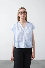 Blusa de algodón con rayas verticales celestes y blancas, con apliques florales en relieve blancos. Presenta cuello camisero y escote en V, con mangas cortas y calce holgado.