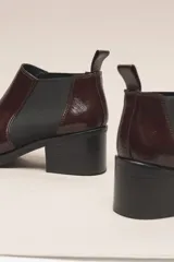 Botín chelsea de cuero vacuno color bordó con acabado charol, punta fina y elástico lateral negro. Posee un taco ancho y bajo de goma.