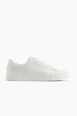 Championes blancos de cuero sintético con suela plana y cordones. Diseño minimalista.