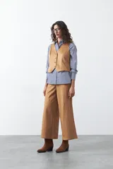 Chaleco de gamuza color marrón, con escote en V y cierre frontal con botones forrados. Tiene un largo a la cintura y silueta definida.