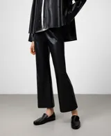 Pantalón negro de efecto cuero, corte flare o acampanado, largo hasta el tobillo. Presenta bolsillos de vivo en la espalda y cierre lateral de cremallera.