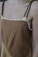Vestido midi de lino color salmón, de corte amplio y silueta holgada. Presenta diseño con cortes irregulares y detalles de pasamanería en el escote y costuras. Cuenta con breteles dobles tipo cuerda y ruedo asimétrico.