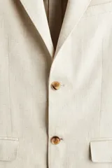 Blazer de botonadura sencilla confeccionado en una mezcla de lino y lyocell. Presenta solapas de pico, cierre frontal de dos botones, bolsillos delanteros con solapa, bolsillo superior y botones decorativos en los puños. Incluye abertura doble en la parte posterior y forro interior.