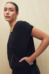 Chaleco color beige sin mangas de silueta relajada, con escote redondeado, cierre frontal con cremallera y ruedo elastizado.