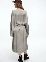 Vestido tipo camisero de corte midi, con cierre frontal de botones, mangas largas amplias y lazo ajustable en la cintura. Presenta un acabado desgastado en tono gris.