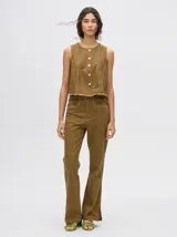 Pantalón de denim color marrón, de tiro alto y calce ochentoso con terminación estilo oxford. Cuenta con apliques metálicos decorativos alrededor de los bolsillos y a lo largo de las costuras exteriores.